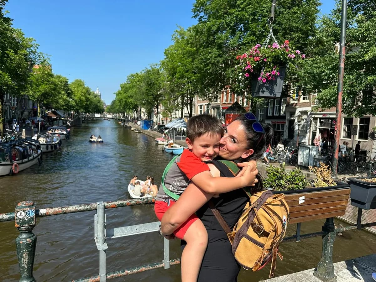 Chiara abbraccia Alessio su un ponte di Amsterdam, con il canale sullo sfondo