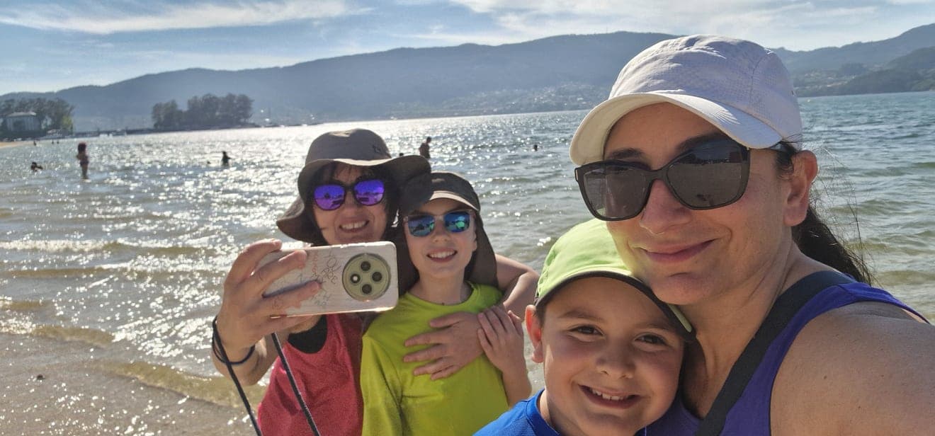 Le due mamme e i due bambini sorridono insieme sulla spiaggia.