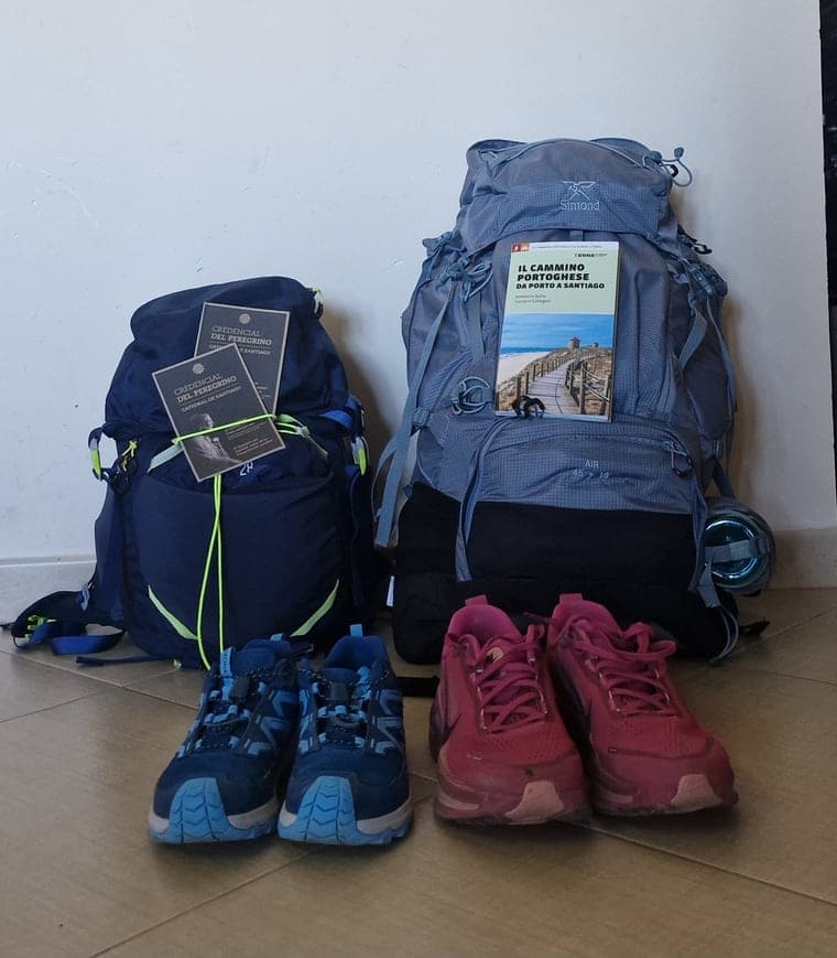 Due zaini con credenziali e guida del Cammino Portoghese, accanto alle scarpe.